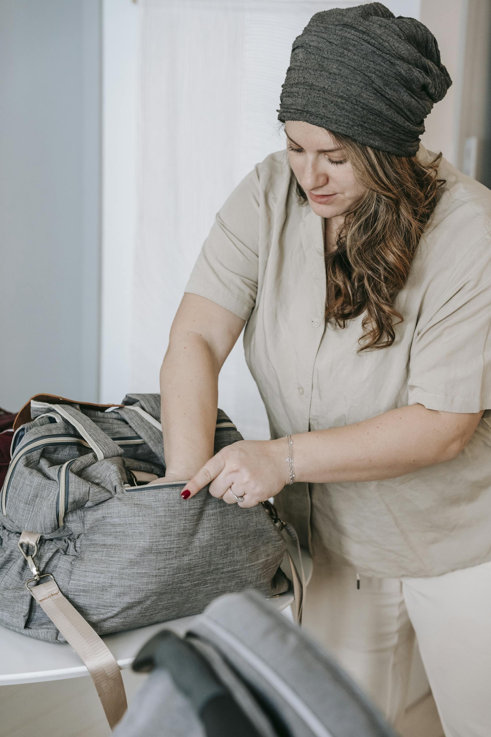 Curve woman in cap packing bag while preparing for stroll with little baby